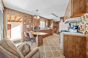 Kitchen featuring wood finish cabinetry, a peninsula, light countertops, wooden walls, and a breakfast bar area