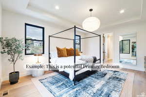 Bedroom with a tray ceiling, light wood-type flooring, ensuite bathroom, and recessed lighting