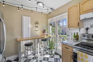 Kitchen featuring light wood finish cabinetry, stainless steel appliances, a breakfast bar and entrance to the rear deck