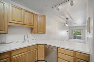 Kitchen featuring stainless steel dishwasher, track lighting, a textured ceiling, and light wood finish cabinets