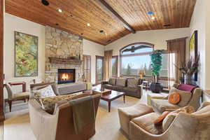 Living room with a high wood beamed ceiling, a stone fireplace, and light colored carpet