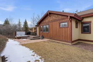 View of snowy exterior featuring a lawn, board and batten siding, a deck, and a jacuzzi