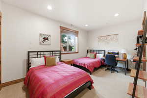 Bedroom with light colored carpet, recessed lighting, and a desk