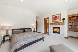 Bedroom with light colored carpet, a tiled fireplace, lofted ceiling, and recessed lighting