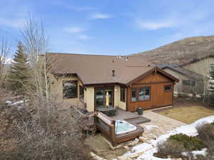 Back of property featuring a hot tub, a shingled roof, and a patio area