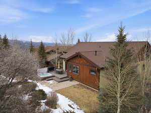 View of side of property with a shingled roof, a hot tub, board and batten siding, a patio area, and a deck