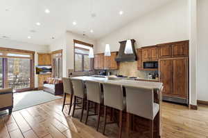 Kitchen with a breakfast bar area, a center island, built in appliances, light wood finished floors, and hanging light fixtures