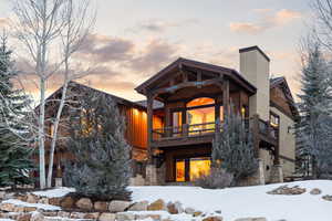 Snow covered rear of property with stone siding, a chimney, and board and batten siding