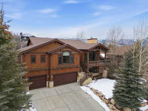 View of front of home featuring an attached garage, a chimney, board and batten siding, driveway, and stone siding