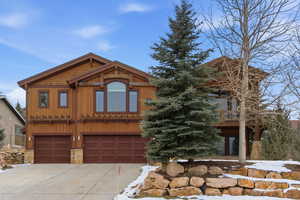 View of front of home featuring an attached garage, concrete driveway, and stone siding