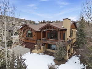 View of front of house featuring an attached garage, stone siding, a chimney, a wooden deck, and board and batten siding