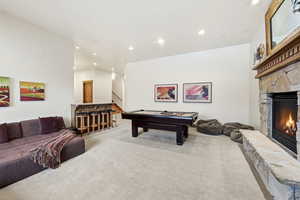 Rec room with a stone fireplace, light colored carpet, billiards table, and recessed lighting