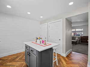 Kitchen with a breakfast bar area, a kitchen island, parquet flooring, a textured ceiling, and gray cabinets