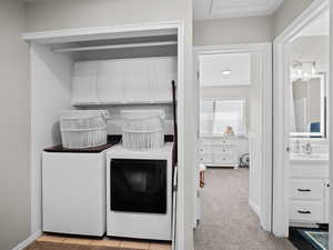 Laundry area featuring light colored carpet, cabinet space, and washing machine and clothes dryer