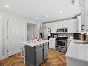 Dual tone kitchen featuring stainless steel appliances, a kitchen island, parquet flooring, backsplash, and recessed lighting