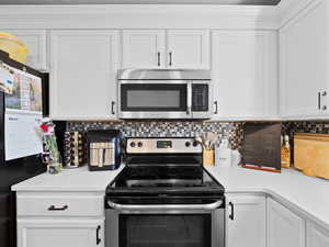 Kitchen with stainless steel appliances, white cabinetry, decorative backsplash, and light stone countertops