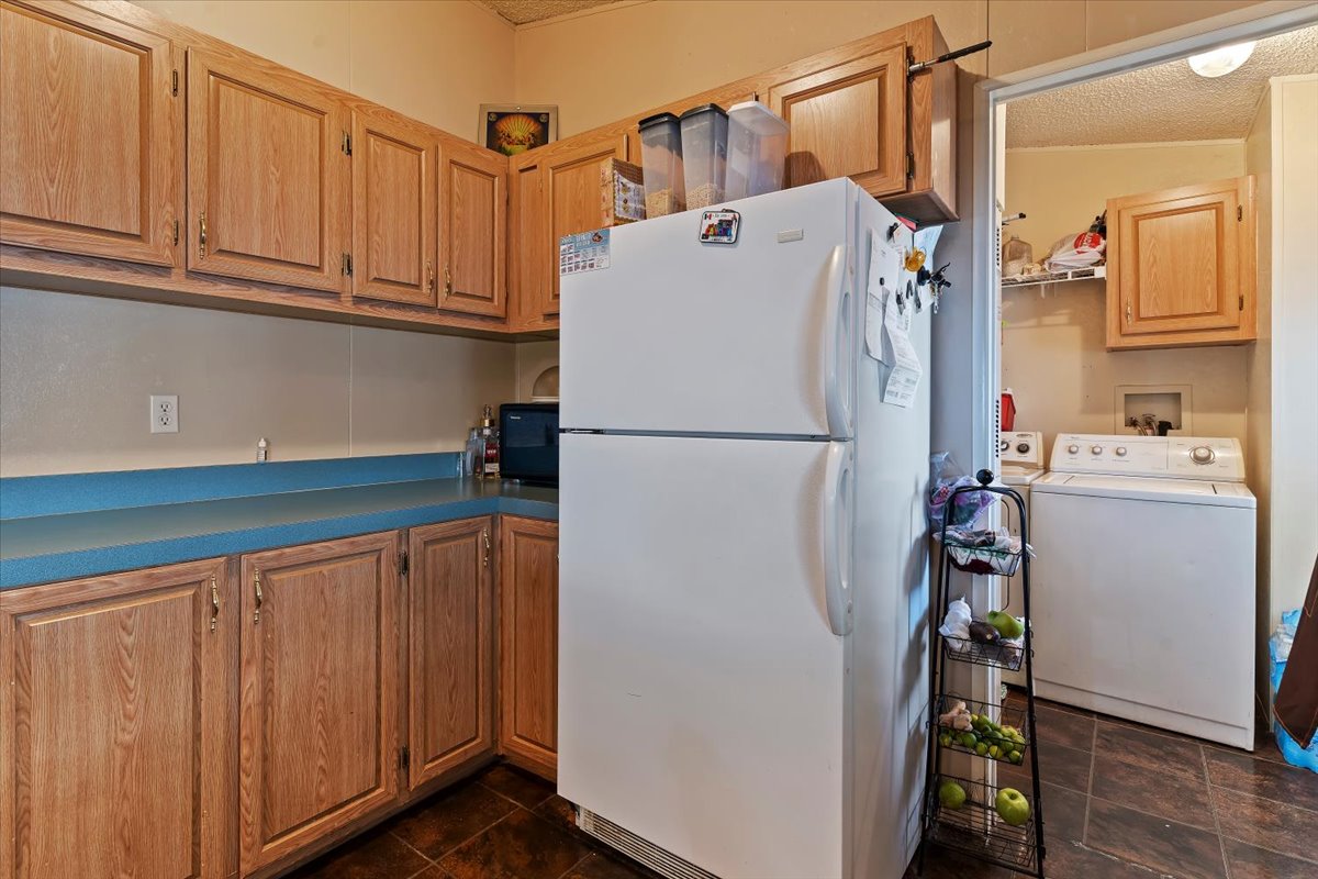 Kitchen with freestanding refrigerator, a textured ceiling, black microwave, dark countertops, and wood finish cabinets
