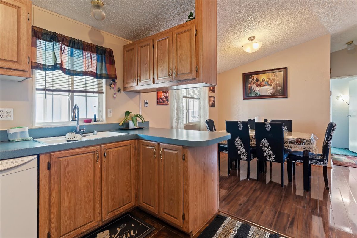 Kitchen featuring dishwasher, a peninsula, wood finish cabinets, dark wood-type flooring, and light countertops