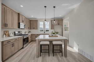Kitchen with stainless steel appliances, a breakfast bar, light wood-style flooring, decorative light fixtures, and a center island