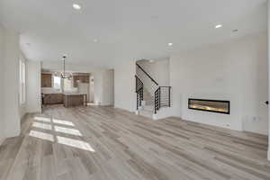 Unfurnished living room with a glass covered fireplace, light wood-style floors, and hanging lights