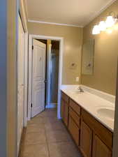 Bathroom featuring double vanity, a stall shower, light tile patterned floors, and crown molding