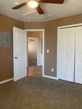 Unfurnished bedroom with dark carpet, electric panel, a closet, and ceiling fan