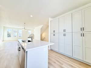 Kitchen with light wood-style flooring, hanging lights, an island with sink, light stone countertops, and dishwasher