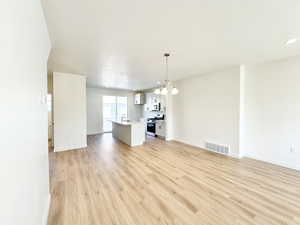 Unfurnished living room featuring light wood-style flooring, suspended lighting, and a textured ceiling
