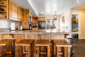 Kitchen featuring a breakfast bar area, black appliances, a peninsula, wood finish cabinets, and dark stone finish floors