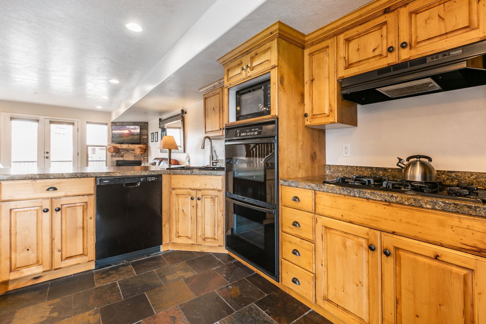 Kitchen with black appliances, dark countertops, stone tile flooring, recessed lighting, and open floor plan