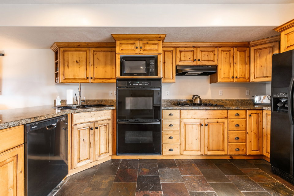Kitchen with black appliances, stone tile flooring, and wood finish cabinets