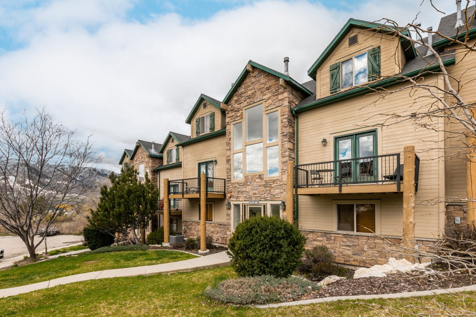 Rear view of property with stone siding, a balcony, and a lawn