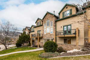 Rear view of property with stone siding, a balcony, and a lawn