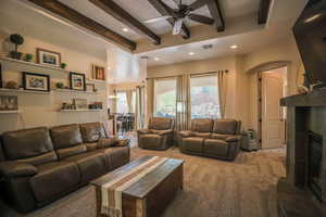 Carpeted living area with a glass covered fireplace, beam ceiling, ceiling fan, and recessed lighting