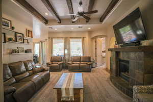 Living room with beamed ceiling, ceiling fan, arched walkways, a tile fireplace, and carpet