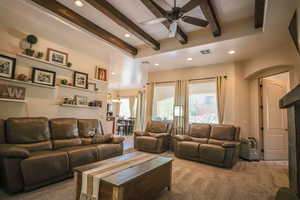 Carpeted living room featuring beamed ceiling, ceiling fan, hanging lights, and plenty of natural light