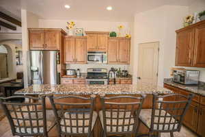 Kitchen featuring stainless steel appliances, dark stone counters, arched walkways, a breakfast bar area, and recessed lighting