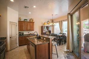 Kitchen featuring suspended lighting, dark stone countertops, a breakfast bar, a center island with sink, and wood finish cabinets