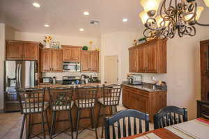 Kitchen with wood finish cabinets, dark stone counters, stainless steel appliances, a kitchen breakfast bar, and an island with sink