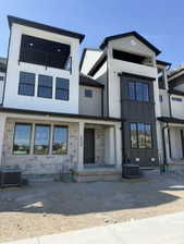 Modern townhome facade featuring a prominent balcony with black railing, light gray brick veneer, dark gray siding, and black-framed windows