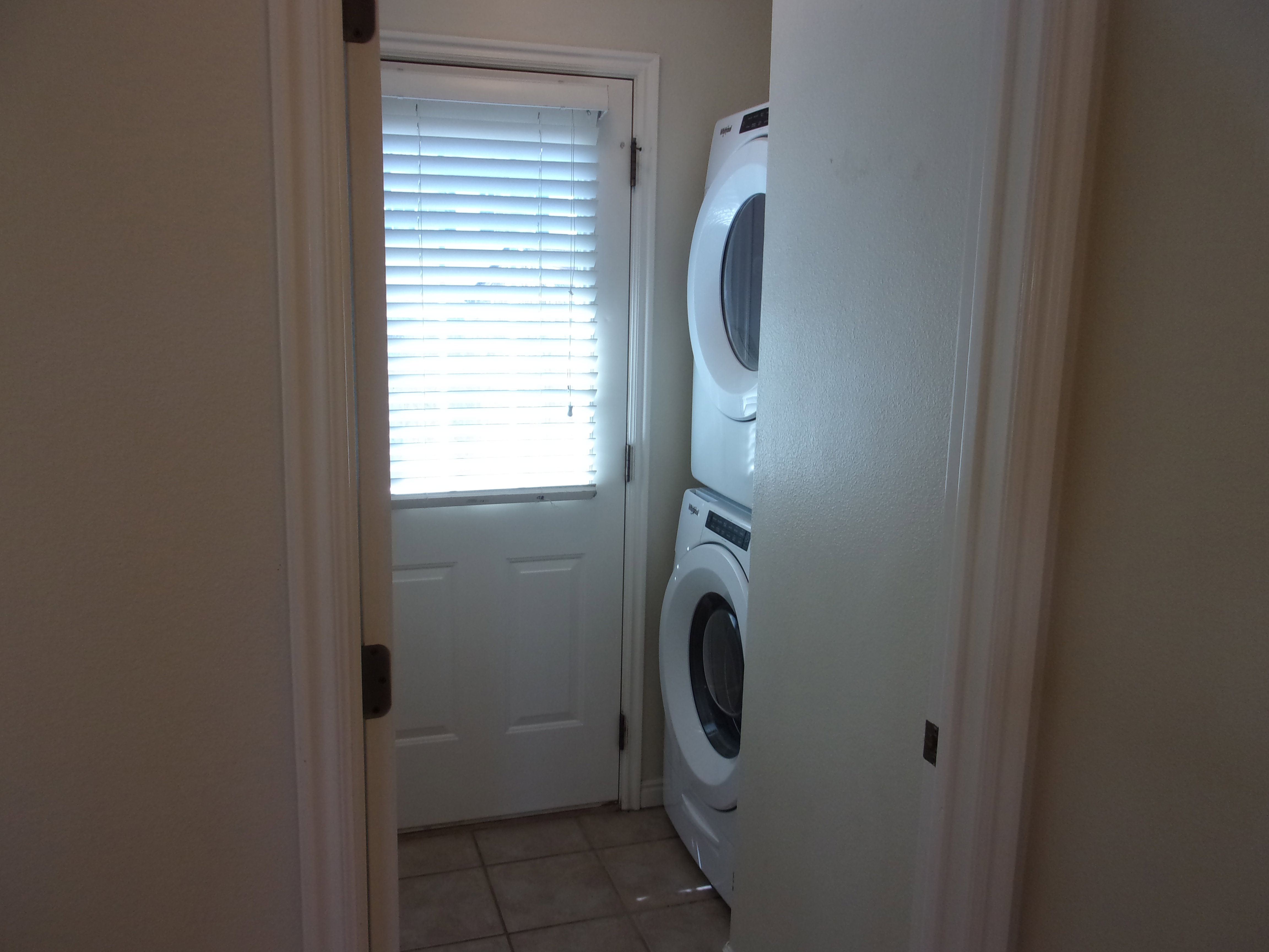 Laundry room with light tile patterned flooring and stacked washing machine and dryer