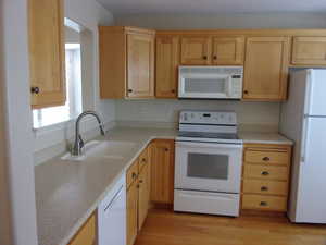 Kitchen featuring light wood finish cabinets, white appliances, light countertops, and light wood-style floors