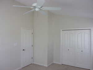Unfurnished bedroom featuring vaulted ceiling, light carpet, a ceiling fan, and a closet