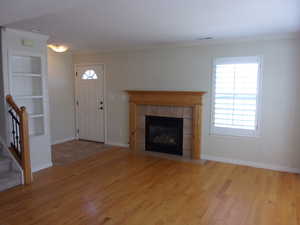 Unfurnished living room featuring built in shelves, light wood-style flooring, crown molding, and plenty of natural light