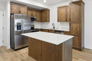 Kitchen featuring stainless steel appliances, a center island, light wood-type flooring, wood finish cabinetry, and light stone countertops