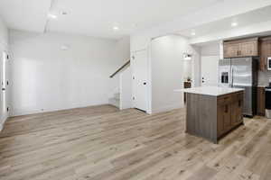 Kitchen with stainless steel appliances, a kitchen island, recessed lighting, light wood-style floors, and light stone countertops