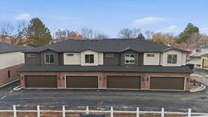 View of front of property featuring roof with shingles, stucco siding, an attached garage, and brick siding