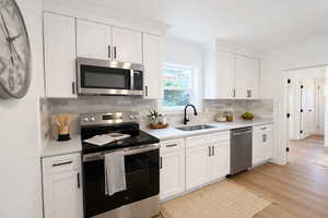 Kitchen featuring stainless steel appliances, white cabinets, light wood-type flooring, tasteful backsplash, and light stone counters