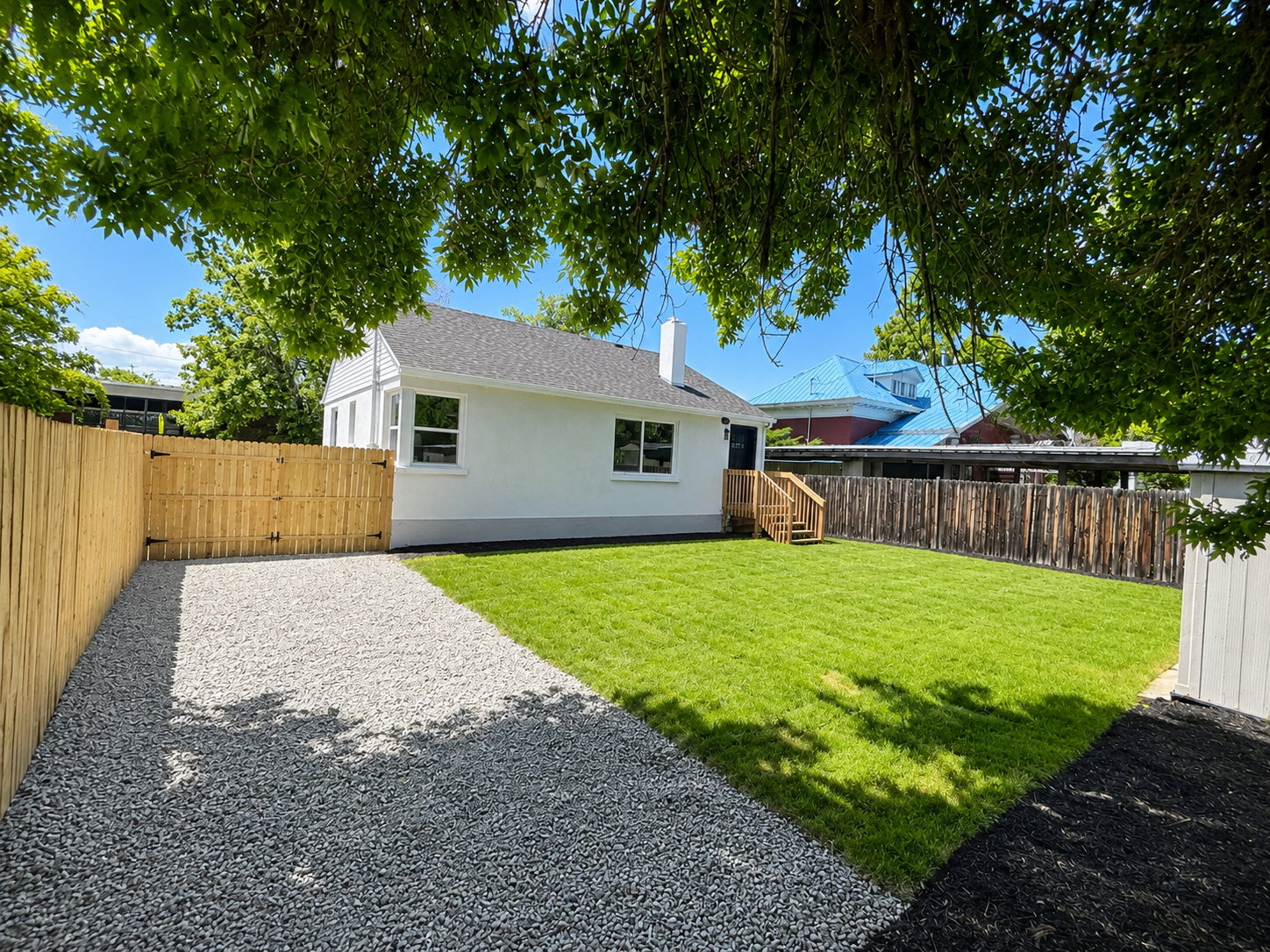 Fenced backyard featuring a gravel driveway, wood deck with stairs, white siding, and a manicured lawn