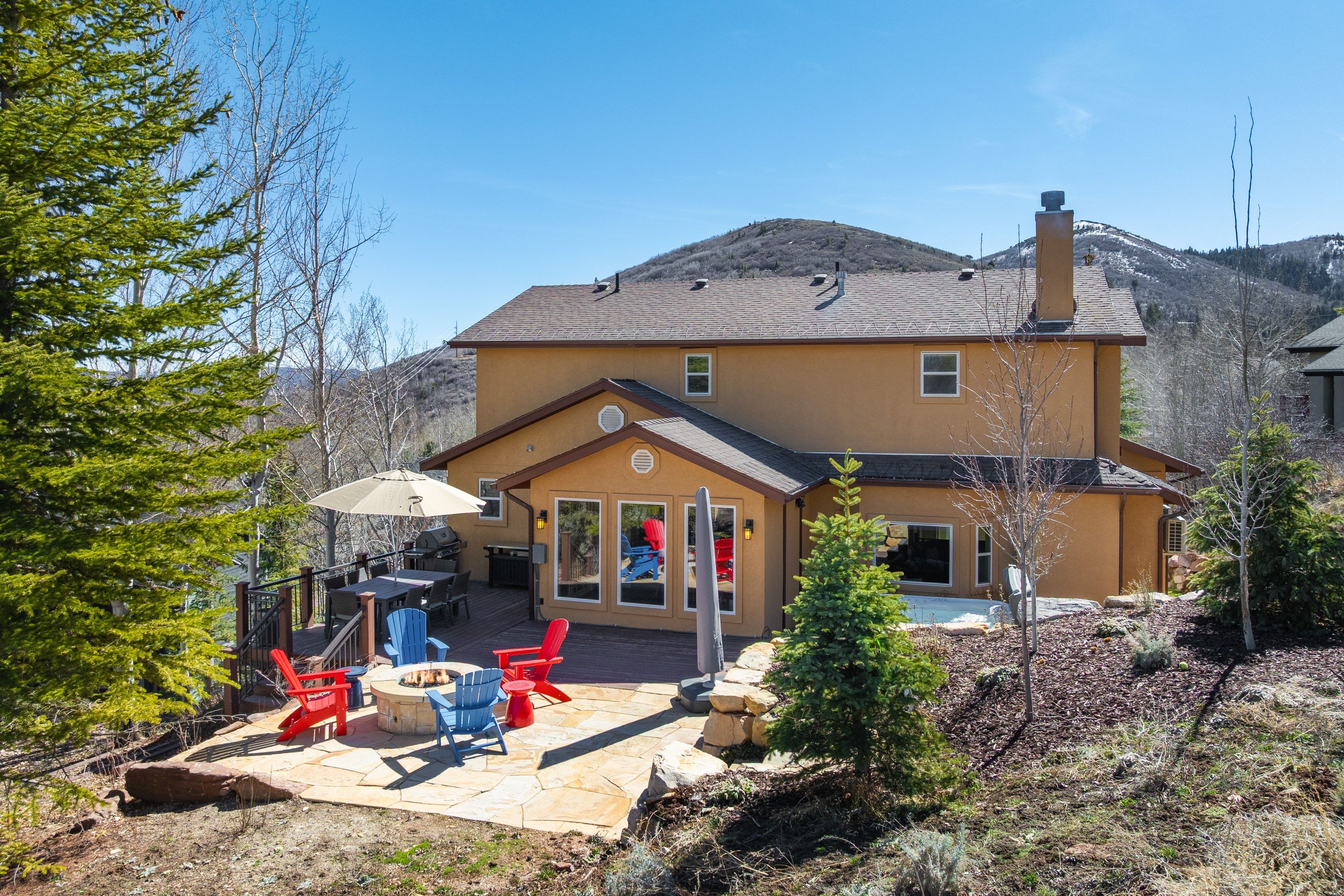 Rear view of house featuring an outdoor fire pit, a chimney, stucco siding, a deck with mountain view, and roof with shingles